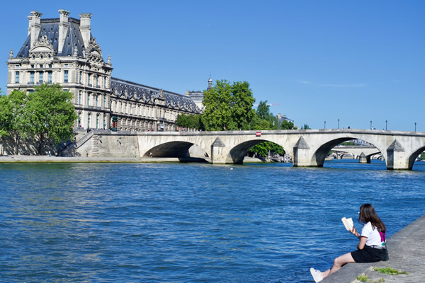 一个女人在法国巴黎的塞纳河河岸上阅读一本书
